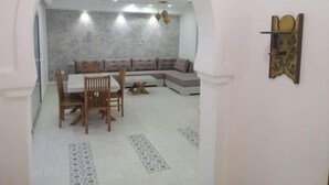 Un comedor con una mesa y sillas blancas, un sofá seccional gris y una alfombra estampada.
