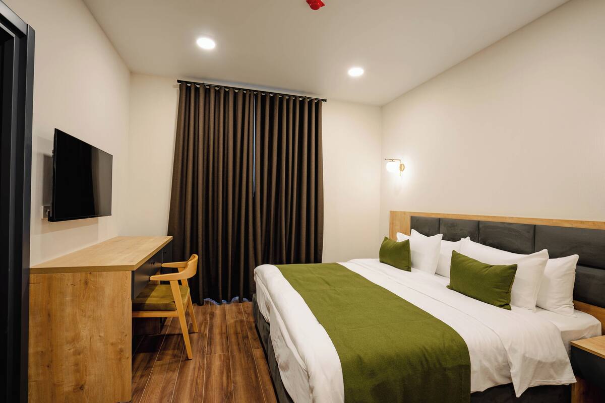 Una habitación de hotel con una cama, un escritorio, una silla, un televisor y una cortina.