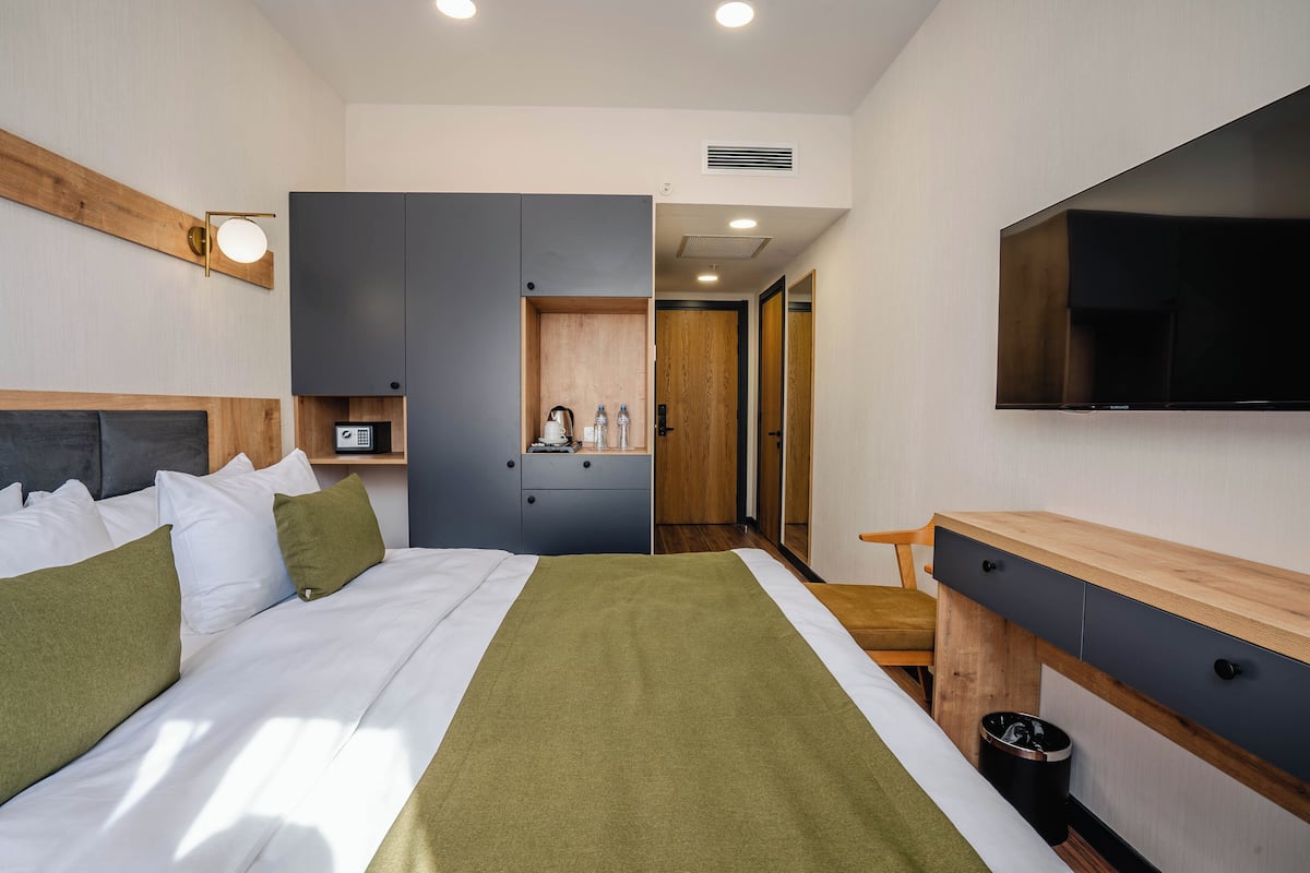 Una habitación de hotel moderna con cama, escritorio, televisor y kitchenette.