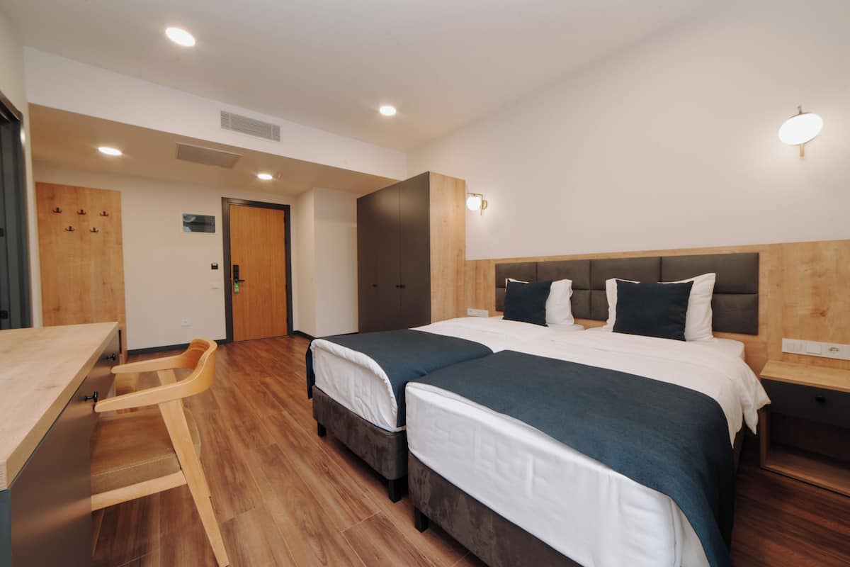 Una habitación de hotel moderna con dos camas, un escritorio de madera y un armario.