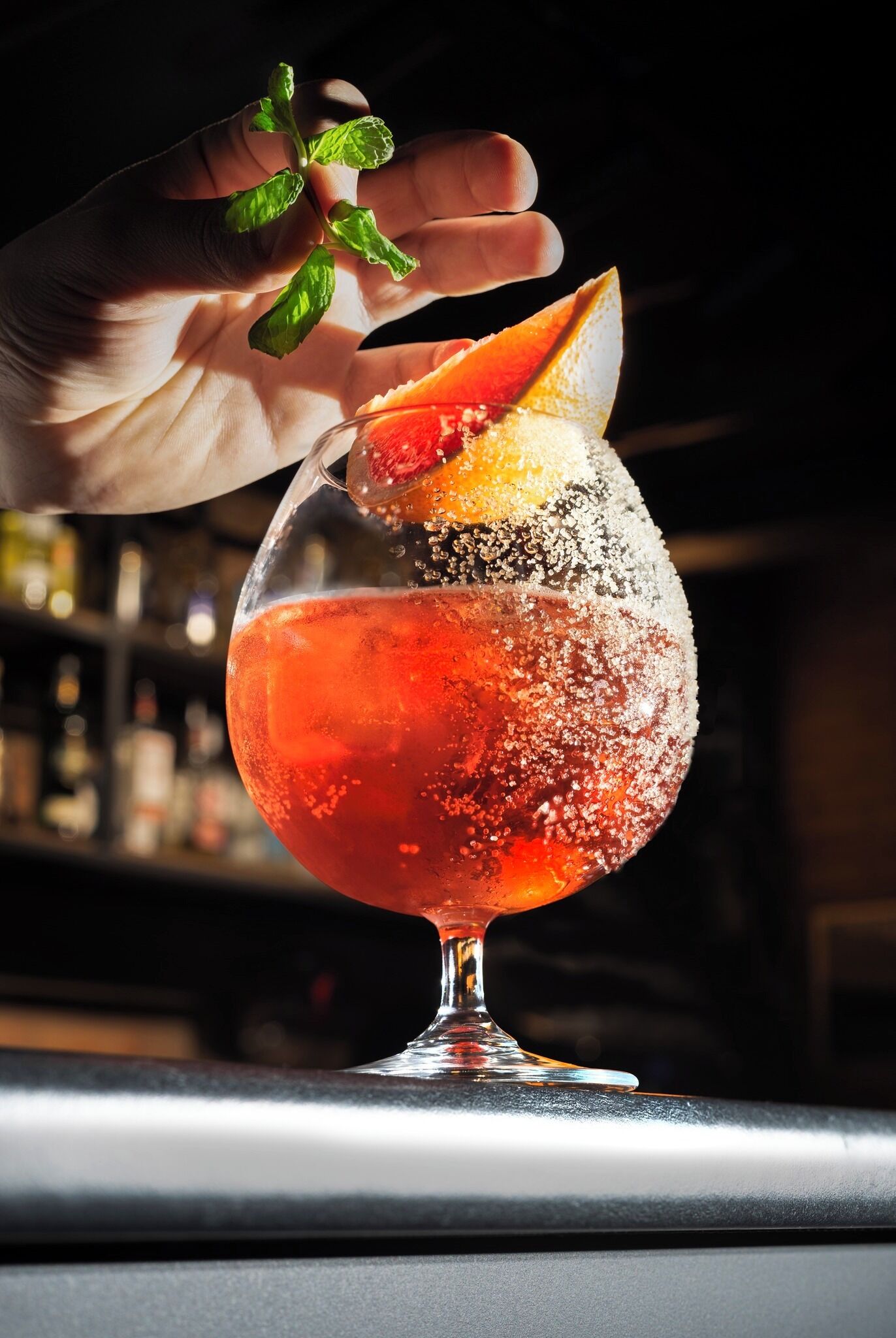 Un cóctel en una copa con rodaja de naranja y ramita de menta.