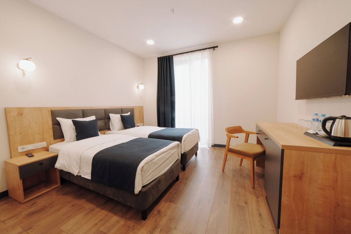 Habitación de hotel con dos camas, un escritorio, una silla, un televisor y una ventana con cortinas.