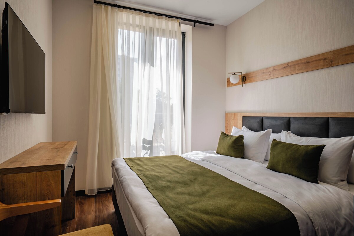 A hotel room with a bed, a desk, a TV, and a window with curtains.