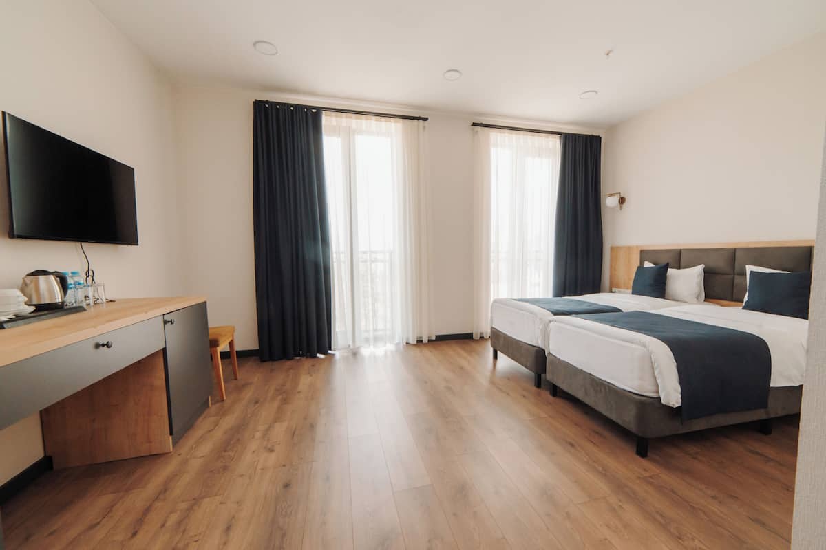Una habitación de hotel con cama, escritorio, televisor y ventana con cortinas.