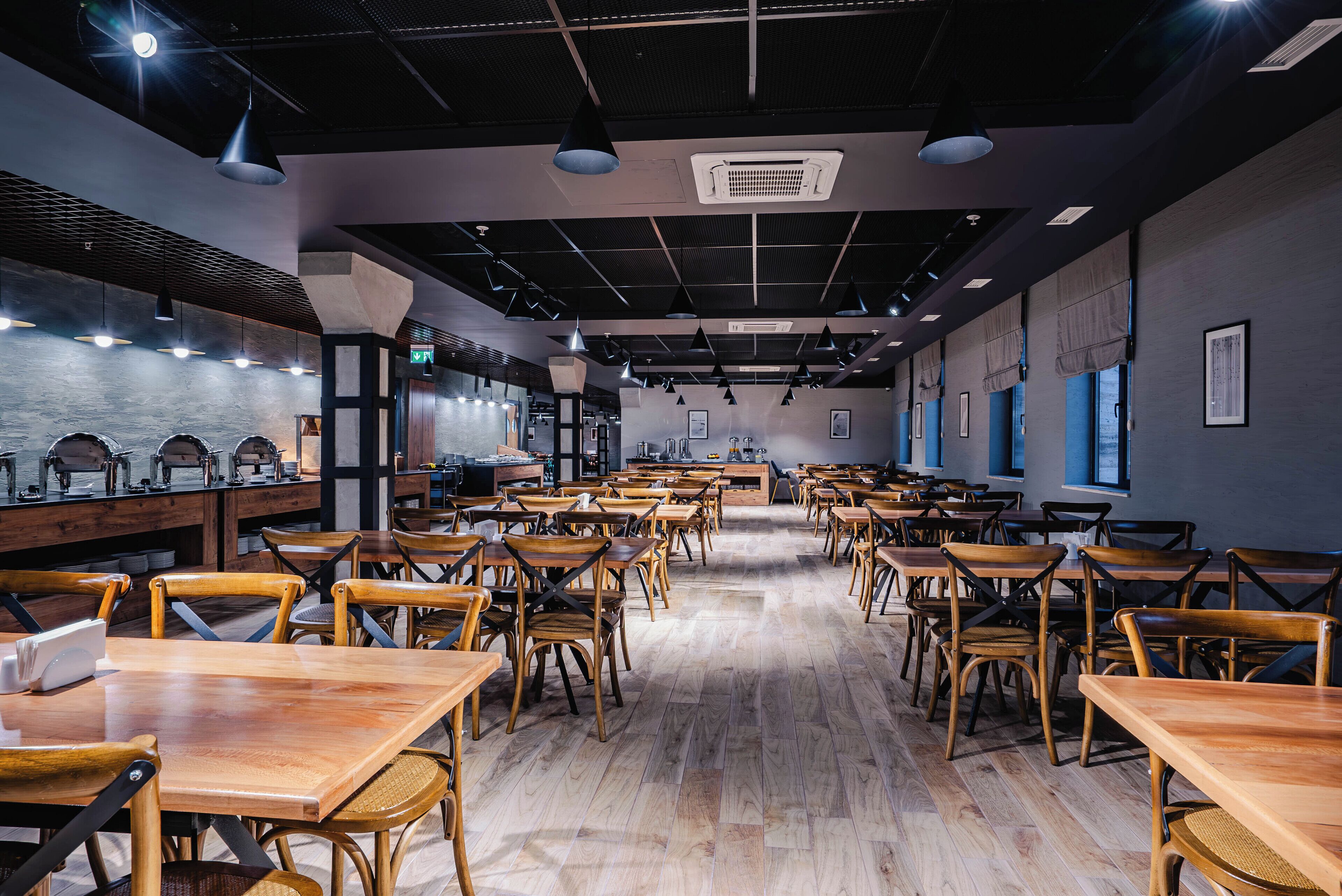 A spacious restaurant with wooden tables and chairs, a high ceiling with exposed beams, and a modern industrial design.