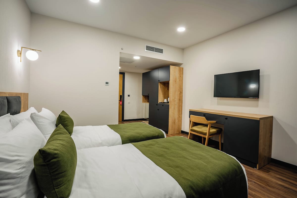 Habitación de hotel con dos camas, un escritorio, una silla, un televisor y un armario de madera.