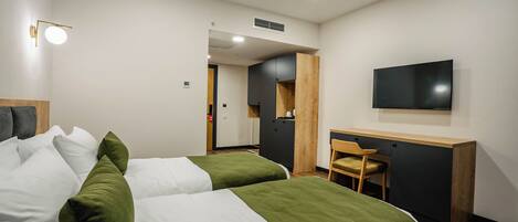 Habitación de hotel con dos camas, un escritorio, una silla, un televisor y una puerta que da a otra habitación.