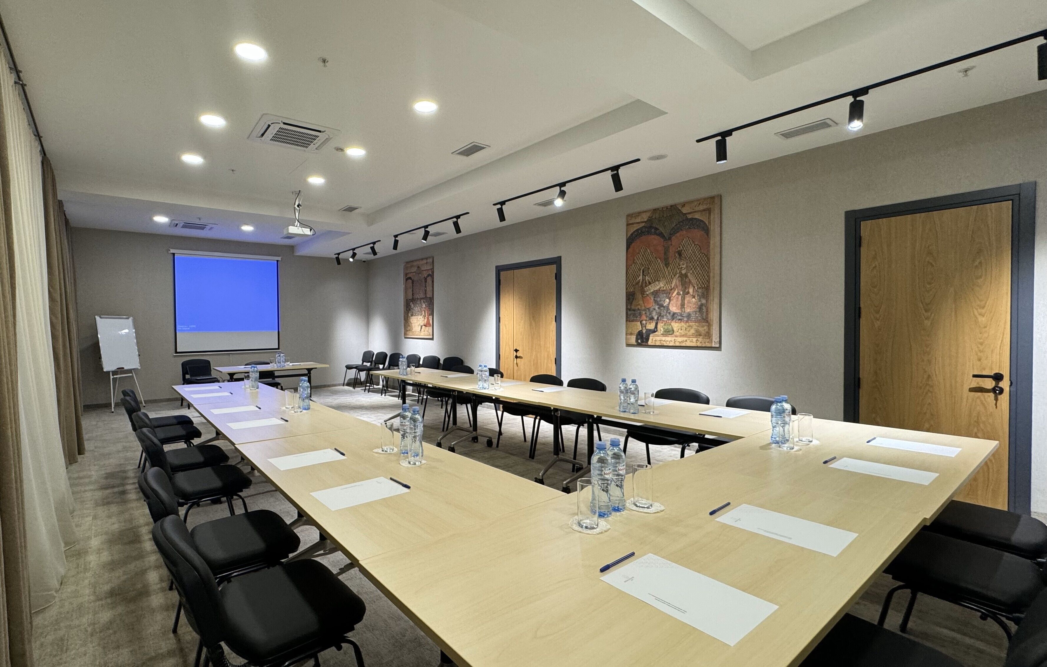 A conference room with a long table, black chairs, water bottles, and a projector screen.