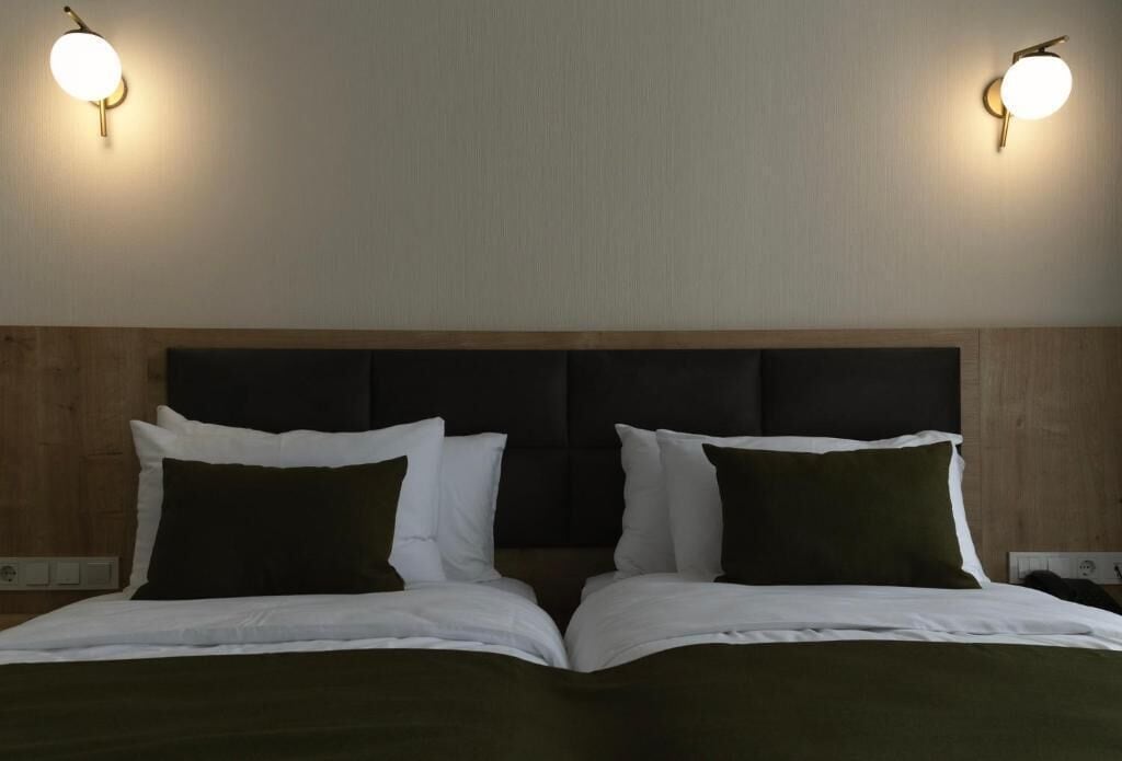 Una cama doble con cabecera oscura, dos mesitas de noche e iluminación empotrada en la pared.