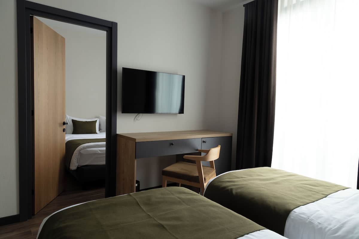 Habitación de hotel con dos camas, un escritorio con silla, un televisor de pantalla plana y una puerta que da a otra habitación.
