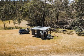 A small cabin with a metal roof, a vehicle parked outside, and a grassy area with trees in the background. - Hermano Farm Stay by Tiny Away (Turill)