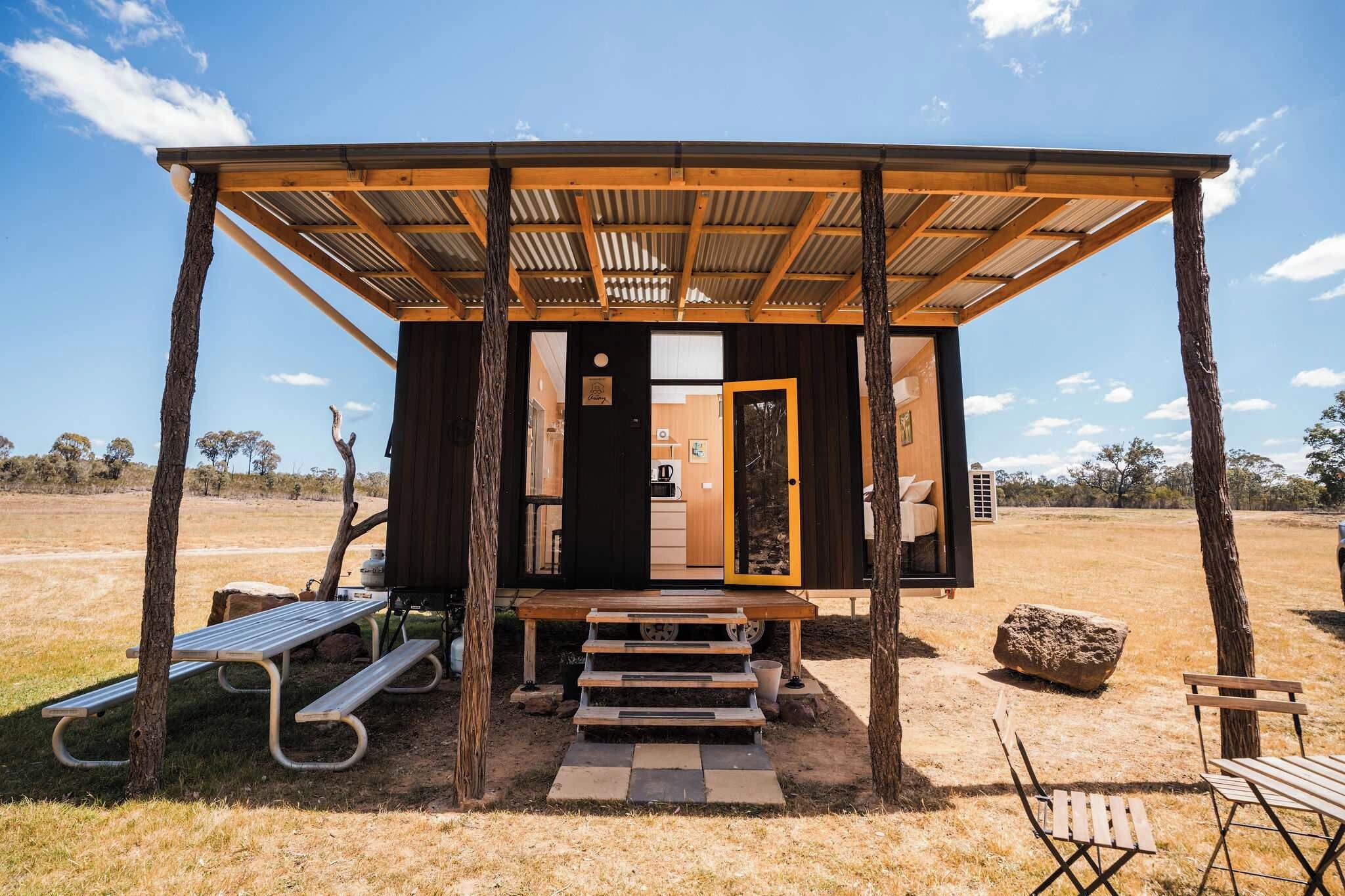 A rustic cabin with a wooden porch, a bench, and a small outdoor seating area.