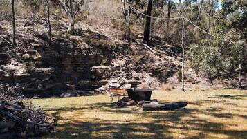 A campsite with a fire pit, a bench, and a picnic table surrounded by dry grass and trees.
