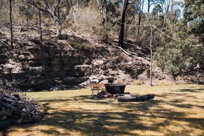 A campsite with a fire pit, a bench, and a picnic table surrounded by dry grass and trees. - Hermano Farm Stay by Tiny Away (Turill)