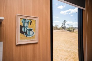 A framed artwork of a coffee pot and cup on a wooden wall, with a view of a dry landscape through a window. - Hermano Farm Stay by Tiny Away (Turill)