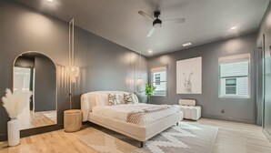 Quarto moderno com cama grande, ventoinha de teto e espelho amplo.