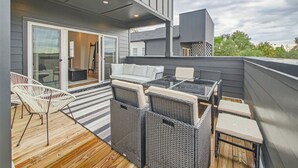 Alpendre coberto com mobiliário de vime, deck de madeira e porta de correr que dá para um espaço interior.