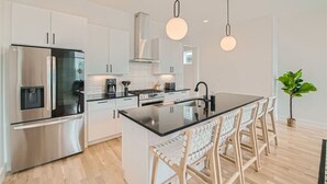 Cozinha moderna com eletrodomésticos de aço inoxidável, uma ilha central com banquetas e iluminação pendente.