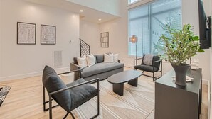 A modern living room with a grey sofa, black armchairs, and a coffee table. There are abstract wall art pieces and a potted plant on a side table. - 24- Home w/  Rooftop- The Music City Collection (Berry Hill)
