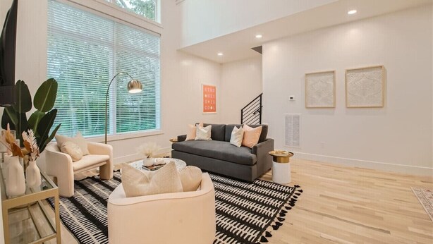 A spacious living room with a large window, a grey sofa, a white armchair, and a black and white rug.
