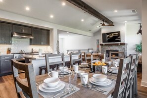 Une cuisine moderne avec des meubles en bois foncé, une cuisinière en acier inoxydable et un coin repas doté d’une grande table dressée pour six personnes.
