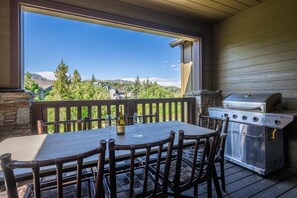Une terrasse extérieure couverte, dotée d’une table et de chaises, d’un barbecue et offrant une vue sur un paysage montagneux.