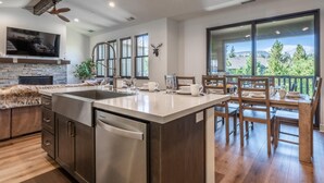 A modern kitchen with a central island, wooden dining table, and large windows offering a view of the outdoors.
