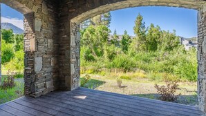 An open stone structure with a wooden deck, surrounded by greenery and a clear sky.