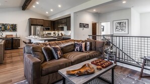 A modern living room with a brown leather sofa, a wooden coffee table, and a staircase with a metal railing.