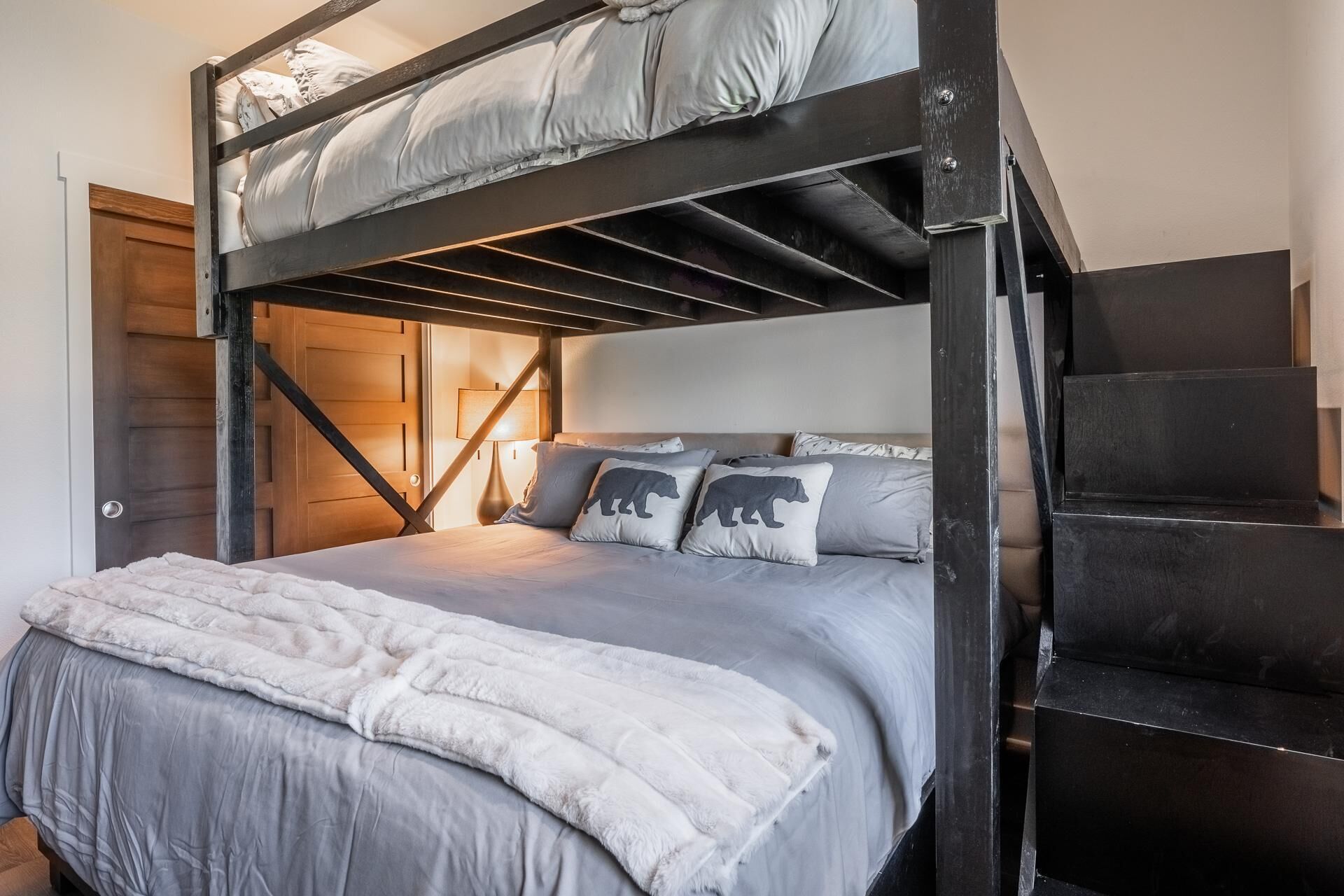 A bunk bed with a grey and white bedding set, a fluffy white throw blanket, and two pillows with bear designs.