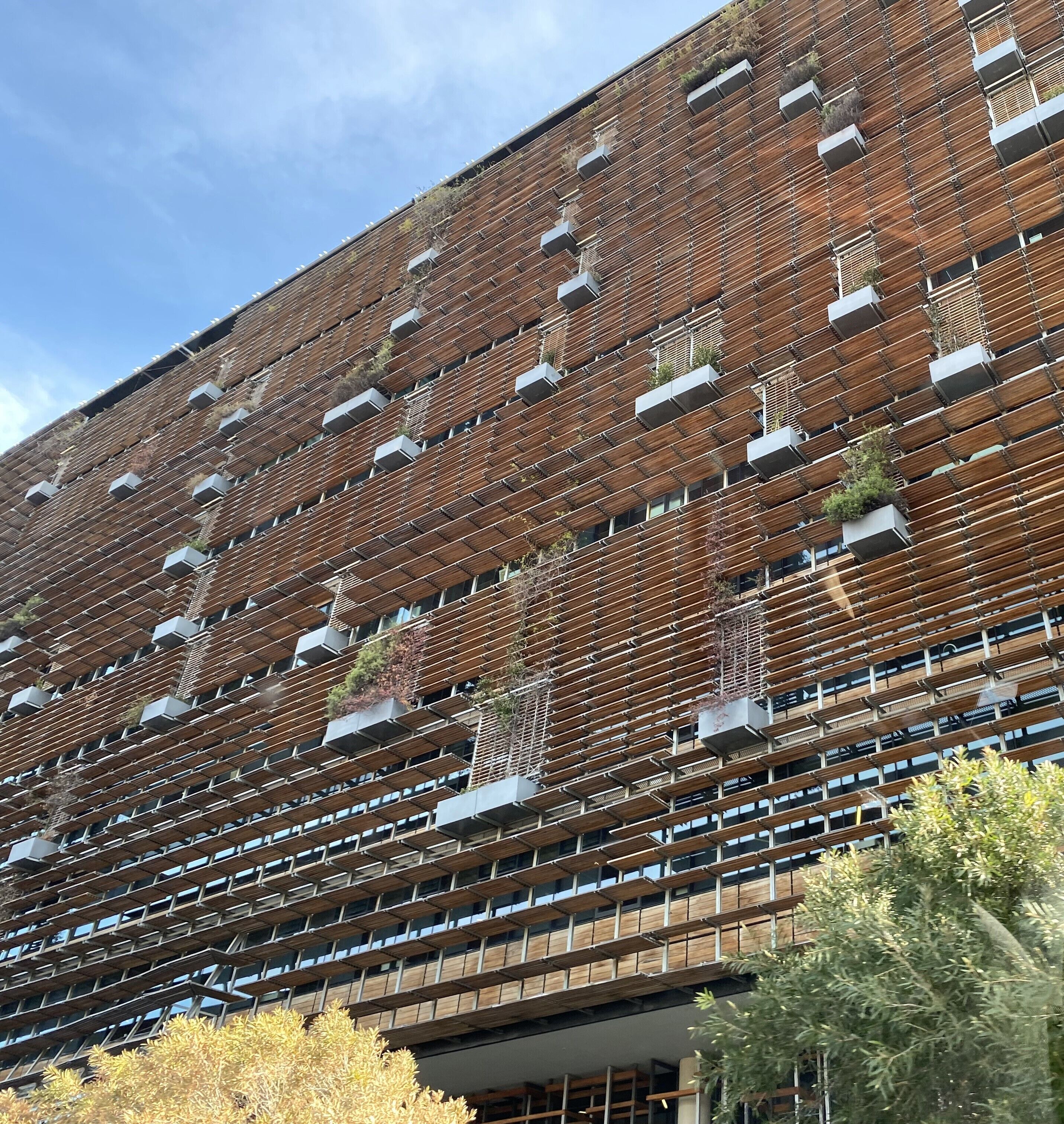 A modern building with a unique facade featuring a grid of wooden slats and air conditioning units.