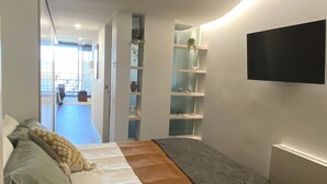 A modern bedroom with a bed, a ceiling fan, built-in shelving, and a TV mounted on the wall. - Sophisticated Lakeview Apt + Parking (Canberra)