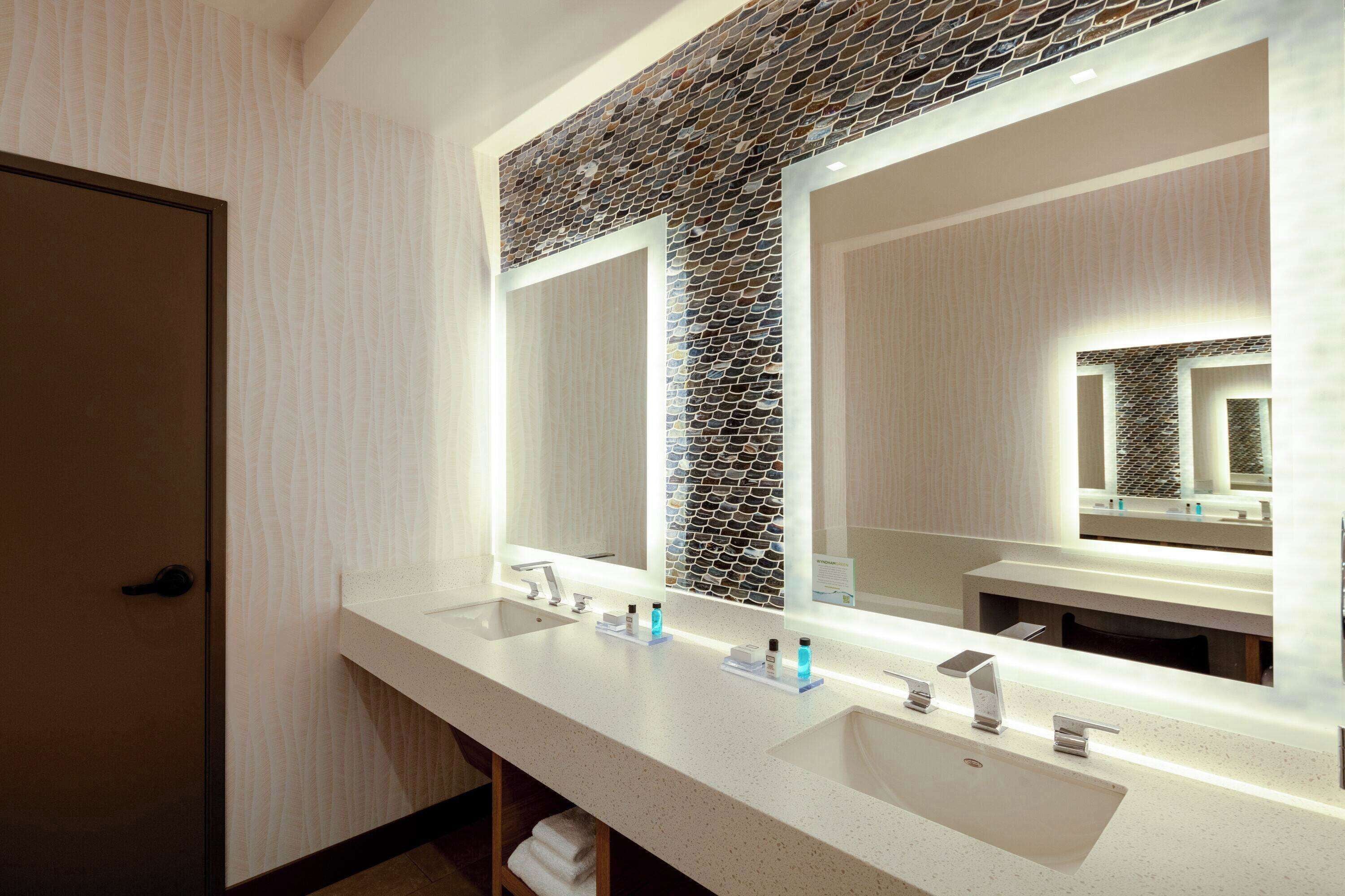 A modern bathroom with two sinks, a large mirror, and a textured wall above the mirror.
