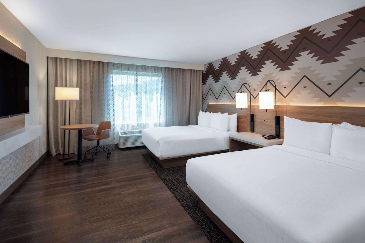 Habitación de hotel con dos camas, un escritorio, una silla, un televisor y una ventana con cortinas.