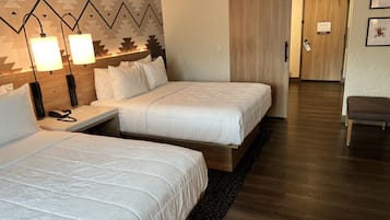 A hotel room with two beds, a desk, and a chair.