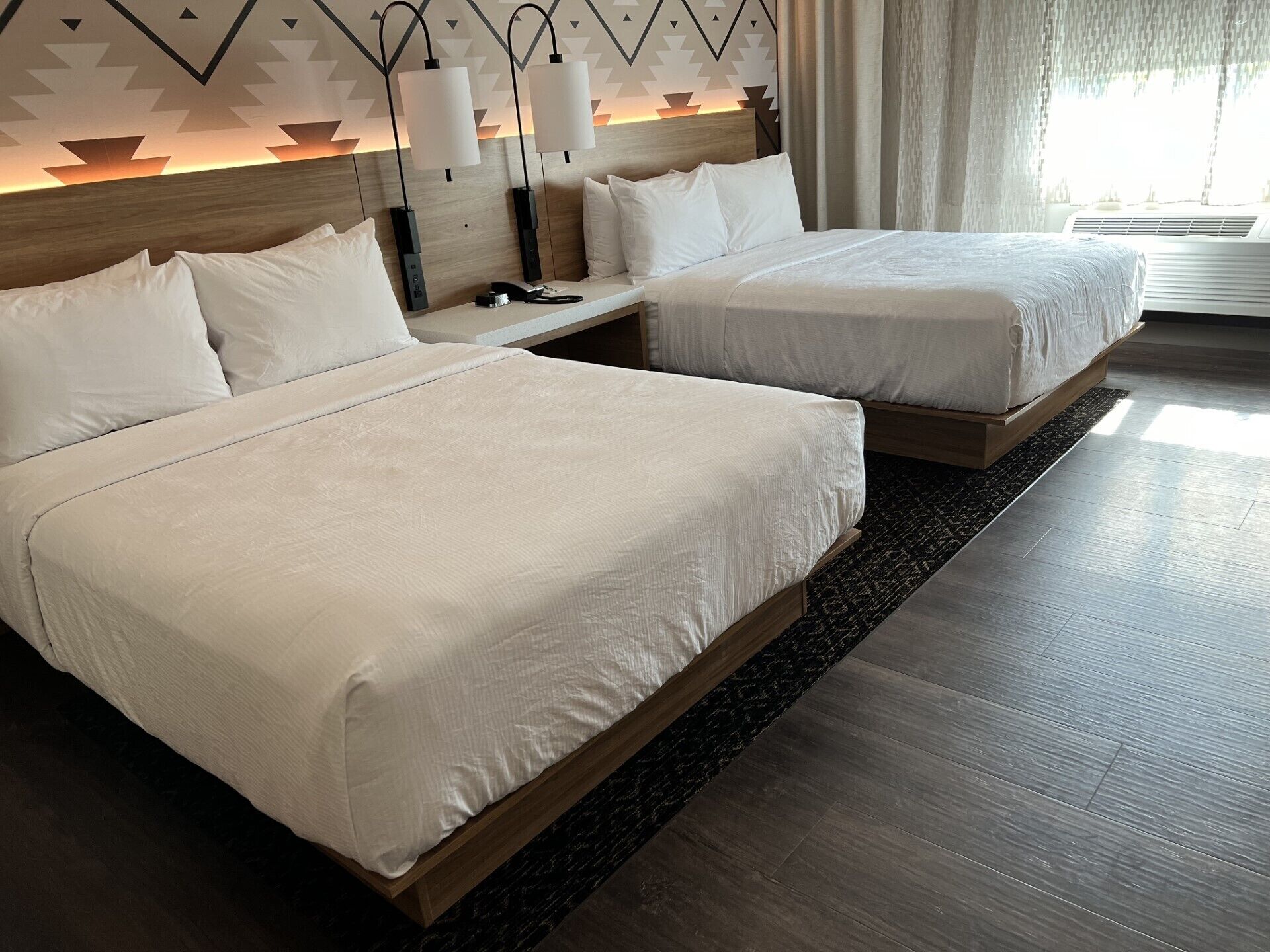A hotel room with two beds, a wooden headboard, and a nightstand with lamps.