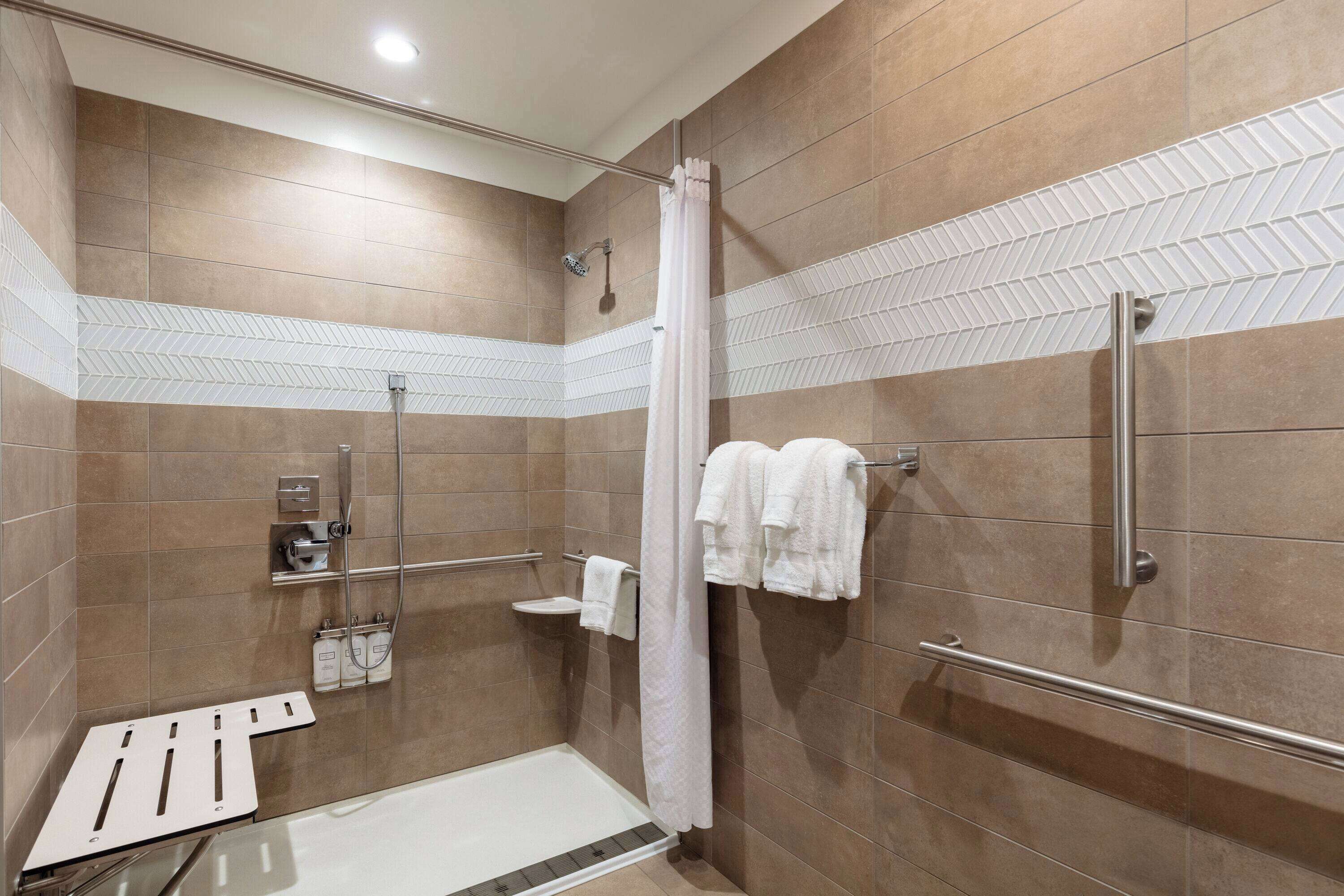 A modern shower area with a glass door, a handrail, and a showerhead.