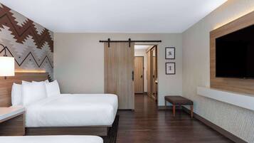 Habitación de hotel con una cama grande, un escritorio, un banco, un televisor montado en la pared y un papel tapiz decorativo.