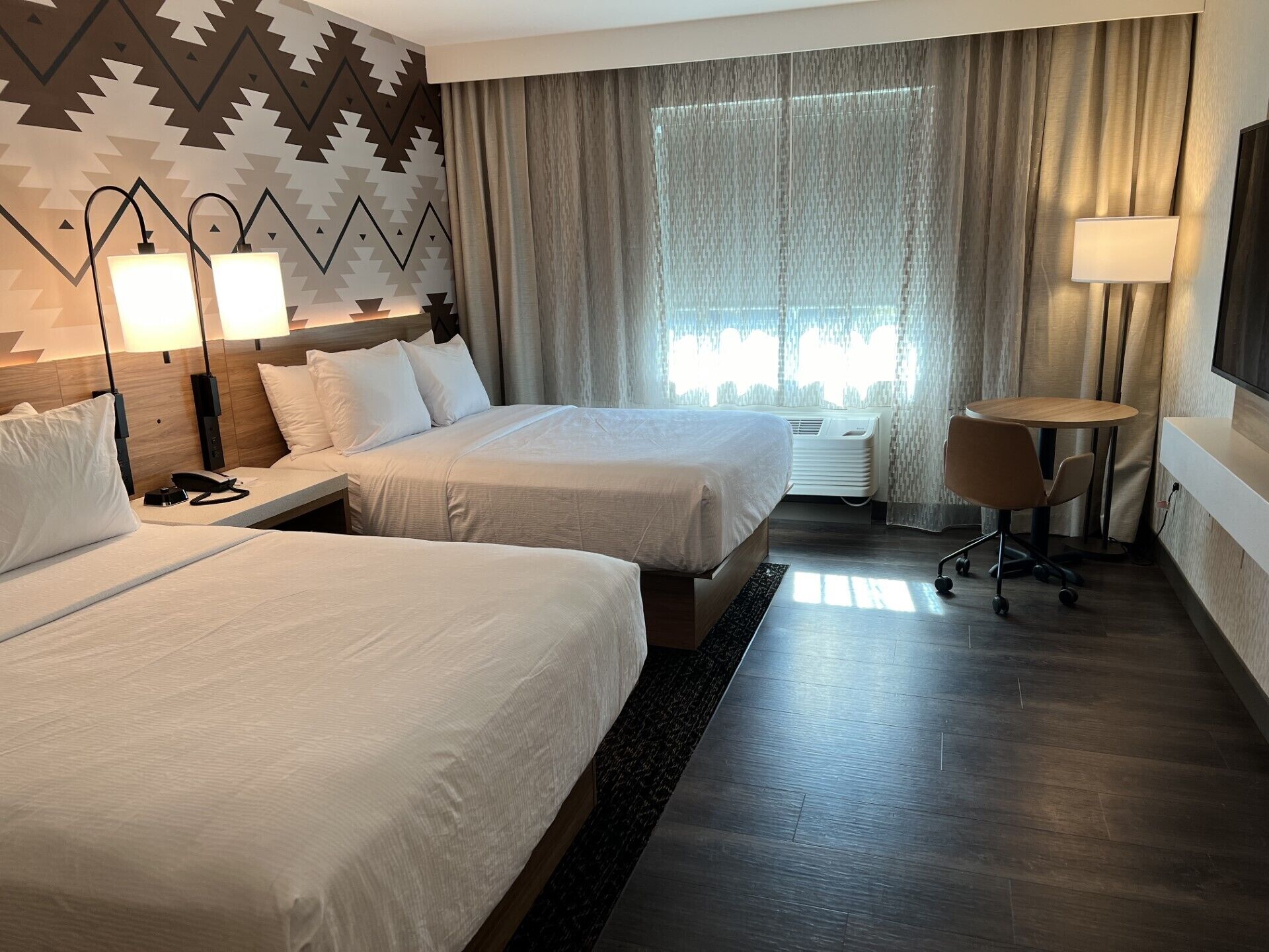 Een hotelkamer met twee bedden, een bureau, een stoel, een televisie en een raam met gordijnen.
