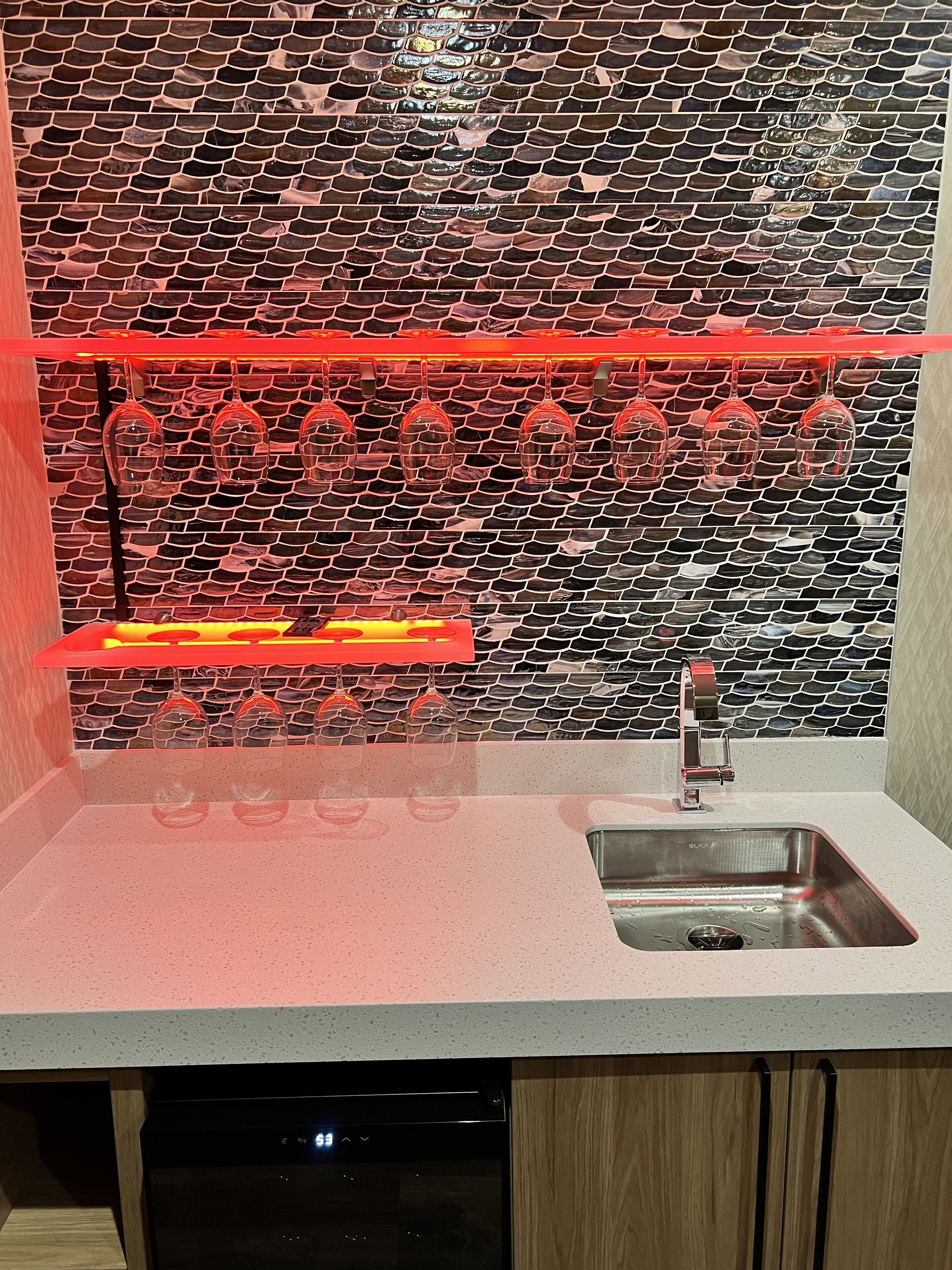 A kitchen with a tiled backsplash, a stainless steel sink, and a dish drying rack.