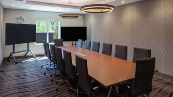 A conference room with a long table, chairs, a clock, and a large screen.