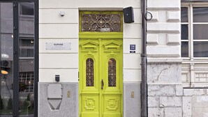 Eine leuchtend grüne Tür mit schmiedeeisernem Gitter, einem Schild mit der Aufschrift „SUPERB“ und der Hausnummer 12 an der Wand.