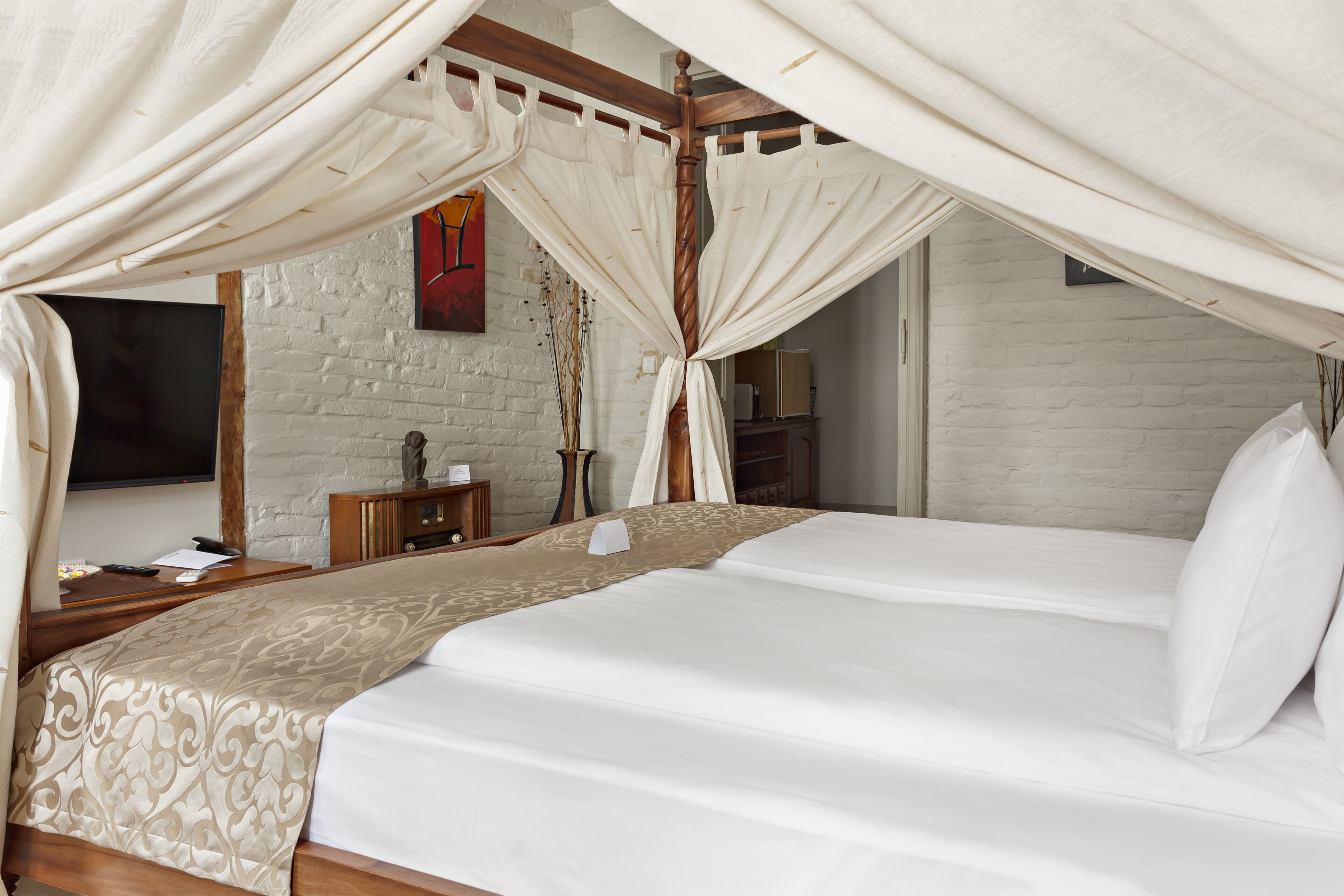 Een slaapkamer met een groot bed, een televisie, een houten nachtkastje en een witte baksteenmuur.