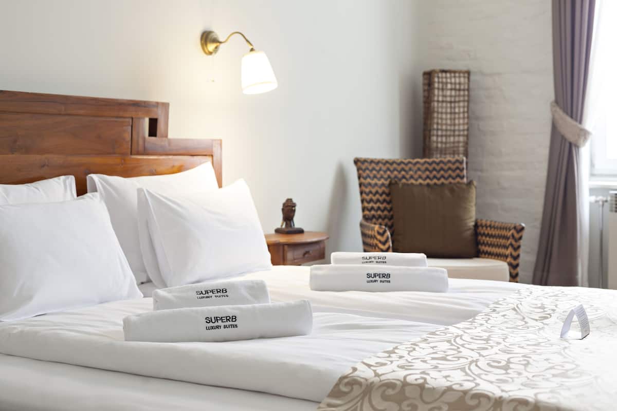 A hotel room with a neatly made bed, a wooden headboard, a lamp, a chair, and a patterned bedspread.