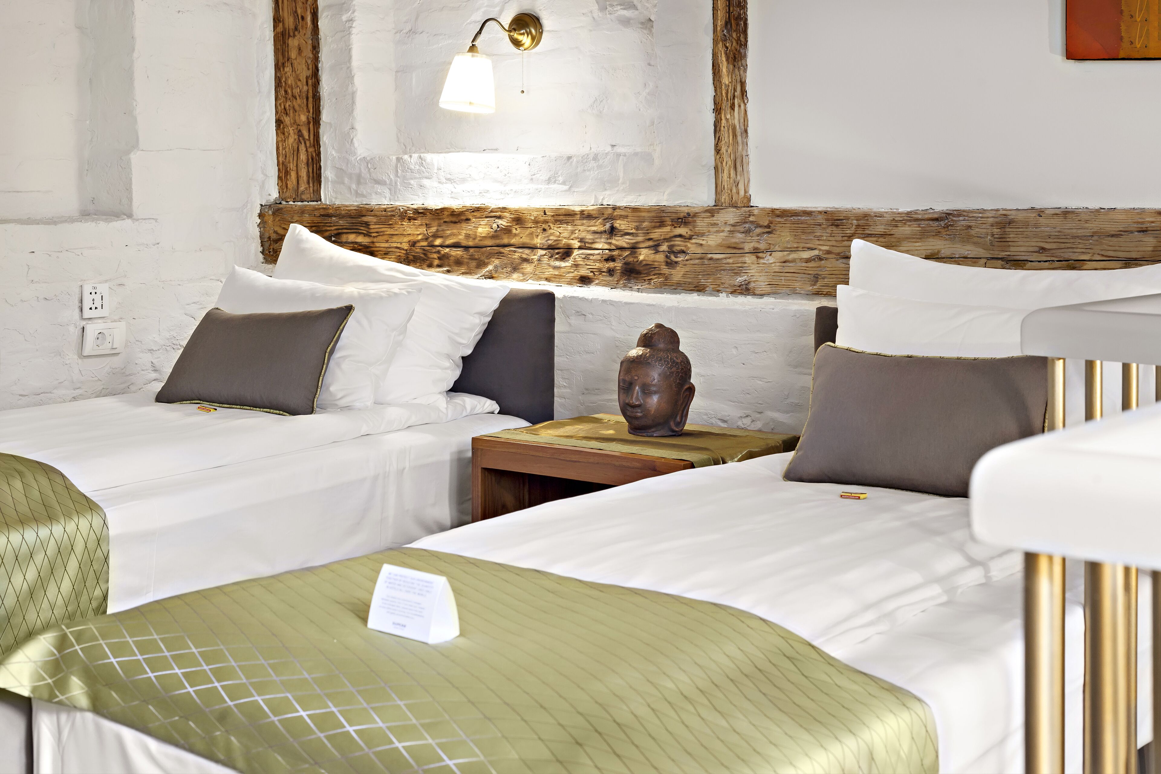 Habitación de hotel con dos camas, cabecero de madera, mesita de noche y lámpara de pared.