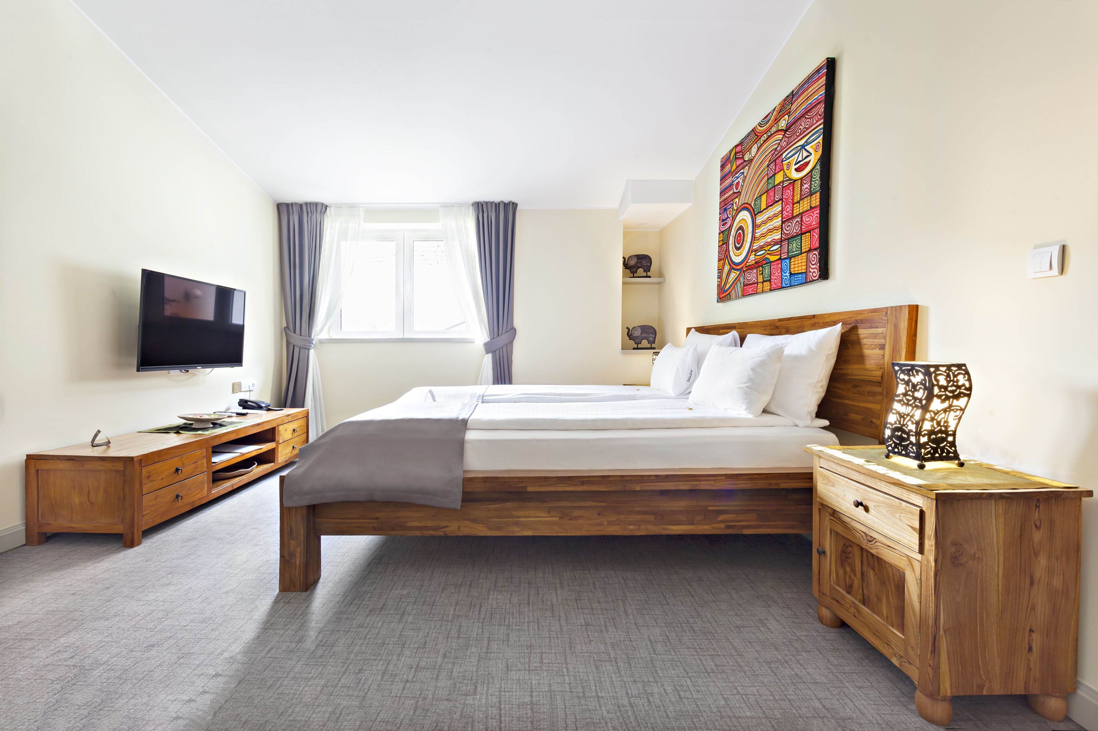 Un dormitorio moderno con una cama de madera, un televisor, una mesita de noche y una obra de arte colorida en la pared.
