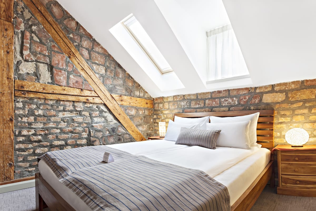 A bedroom with a sloped ceiling, exposed brick walls, a wooden bed frame, and a skylight.