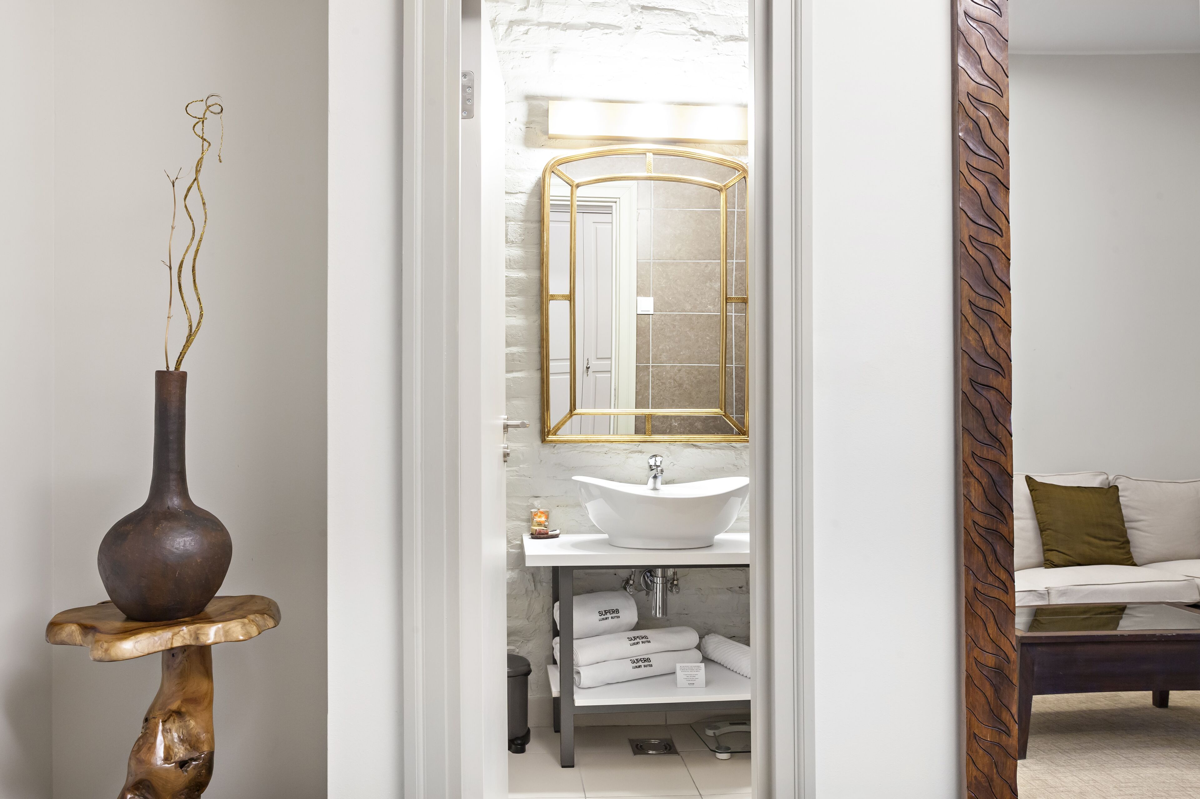 Un baño moderno con tocador blanco, espejo con marco dorado y un florero con ramas.