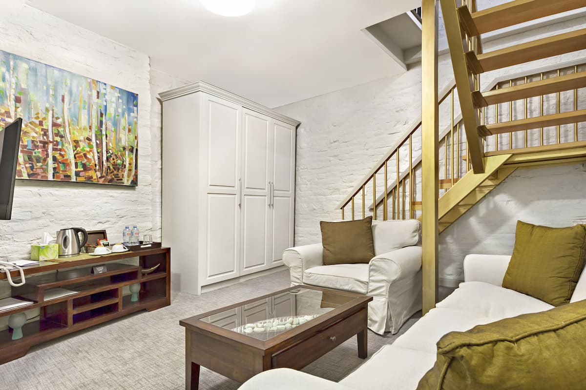 A living room with a white couch, a glass coffee table, a white cabinet, and a staircase with a wooden railing.