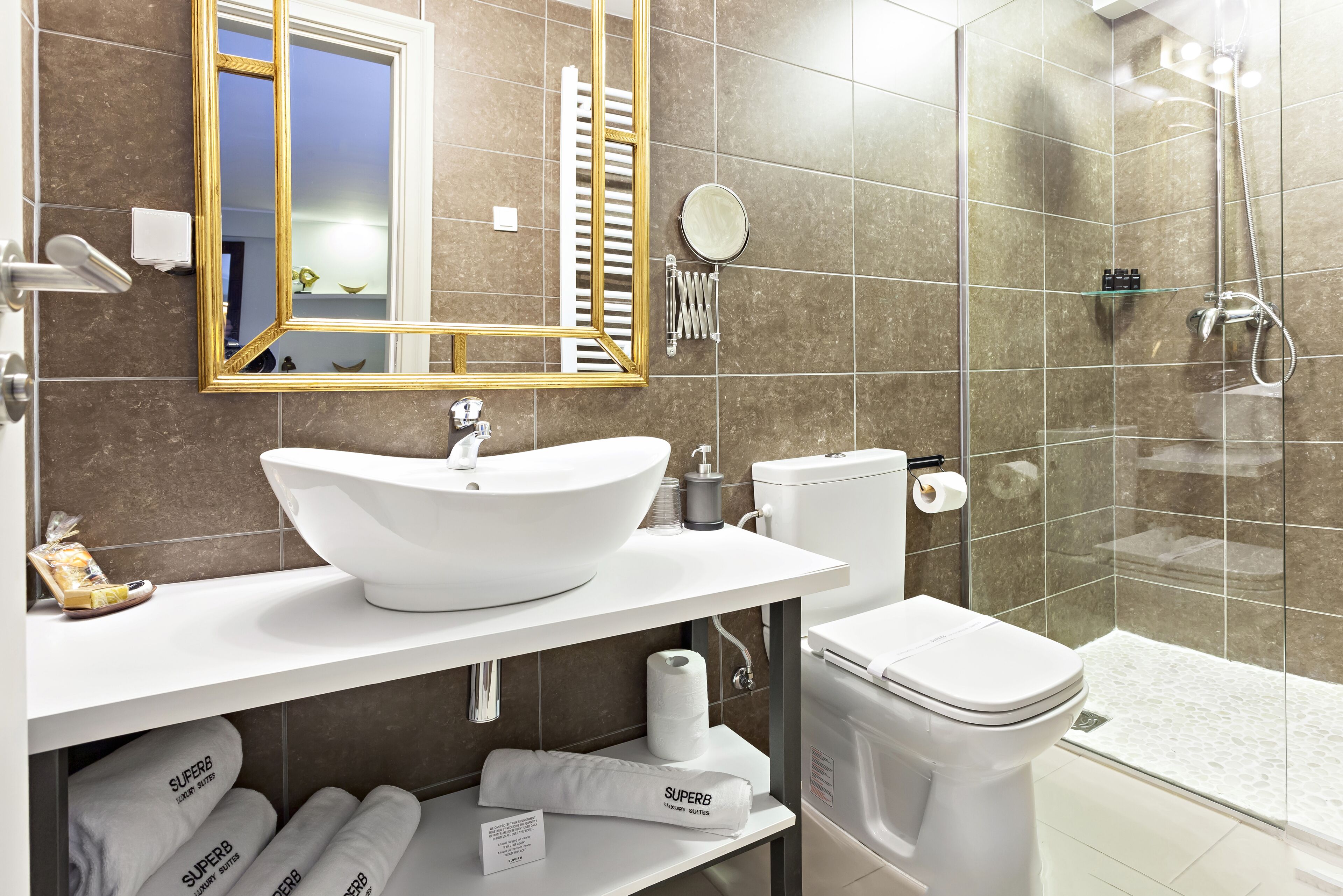 A modern bathroom with a white sink, toilet, and shower. There are towels and toiletries on the counter.
